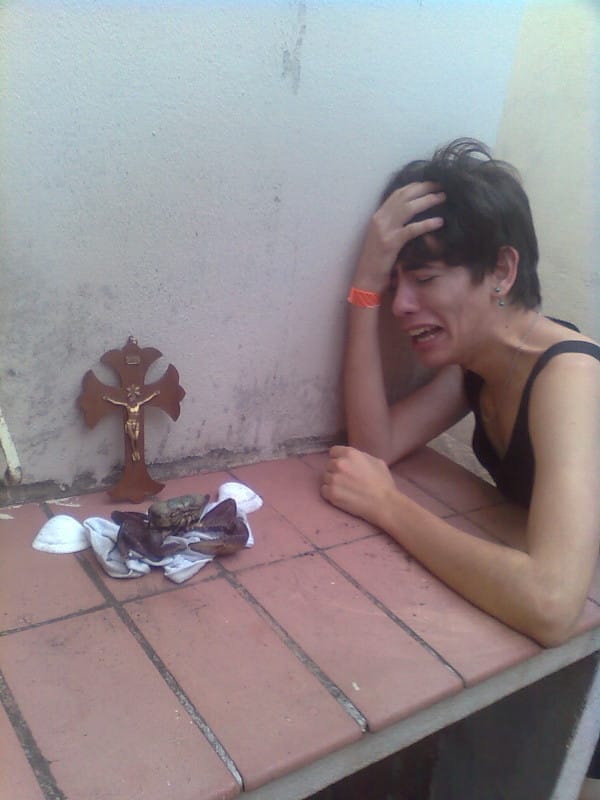 garoto chorando desesperado com a mão na cabeça ao lado de um carangueijo morto e um crucifixo, era o velório do carangueijo