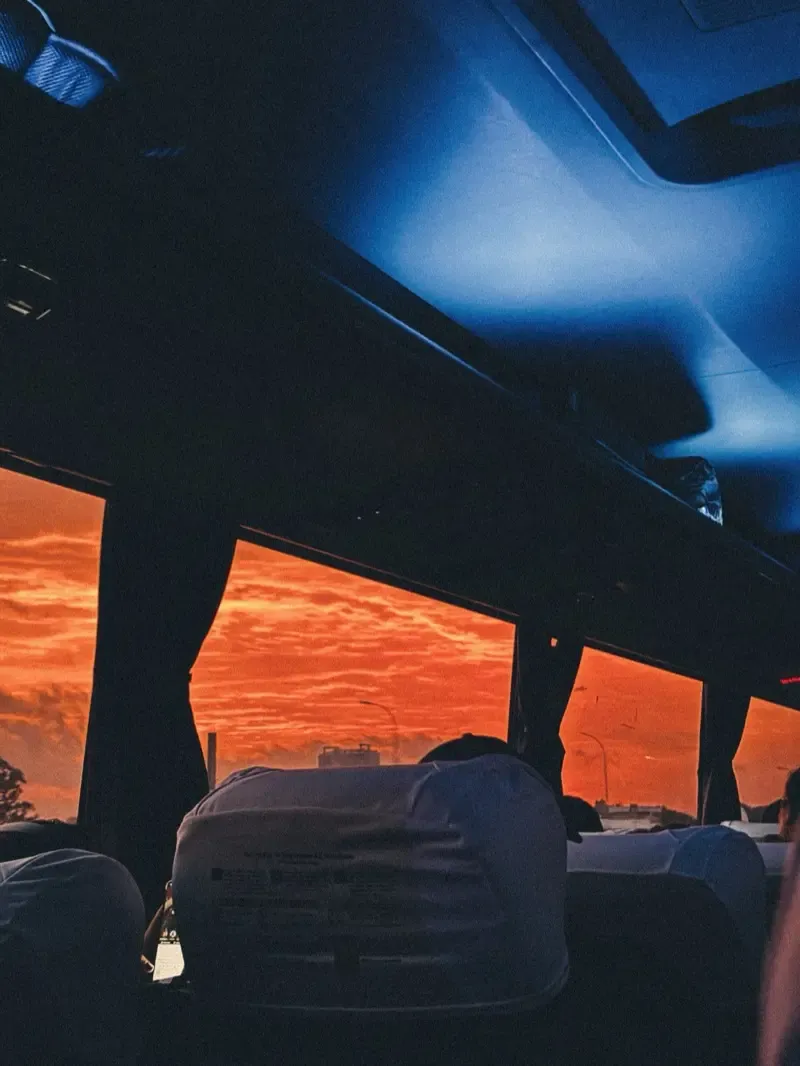 interior de onibus com passageiro observando céu alaranjado através das janelas.