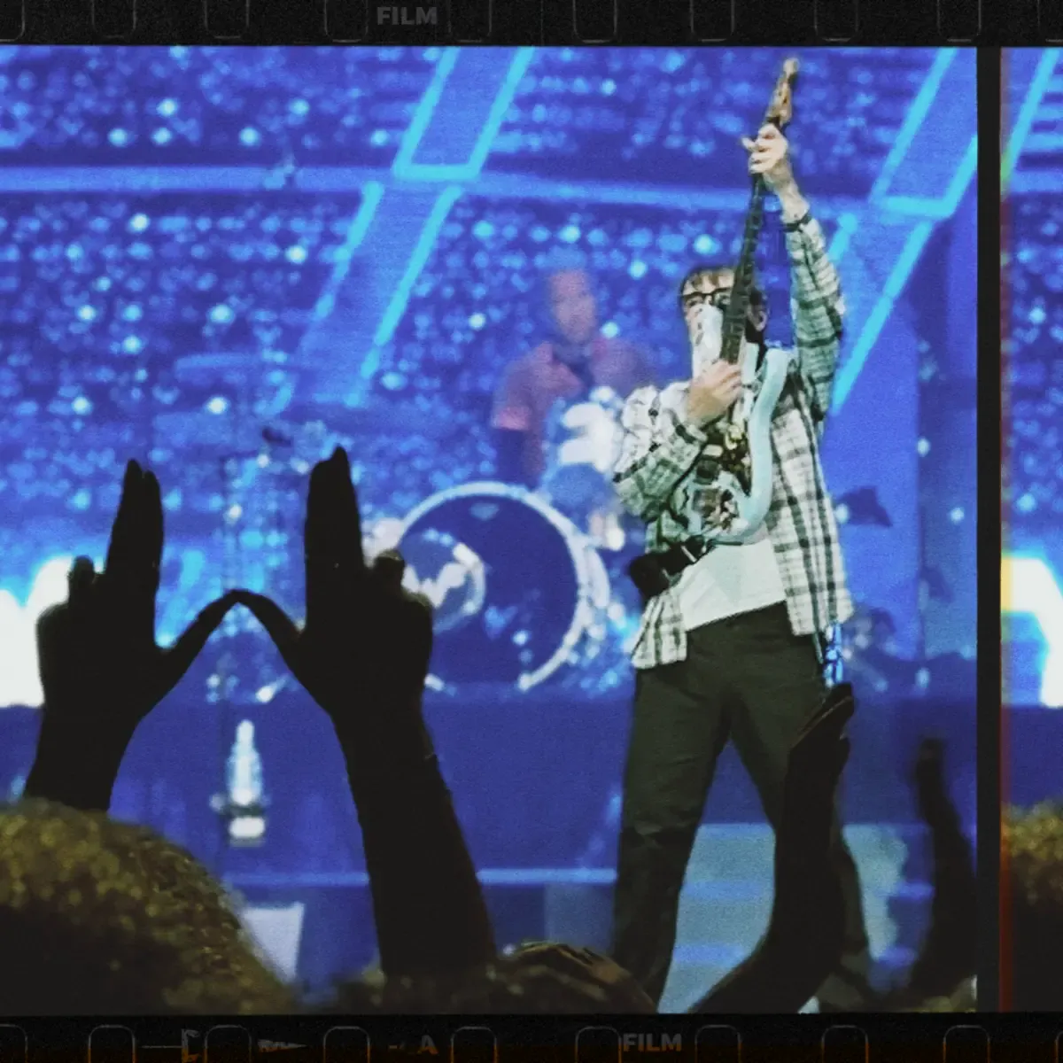 uma mão fazendo W e River Cuomo erguendo guitarra no palco