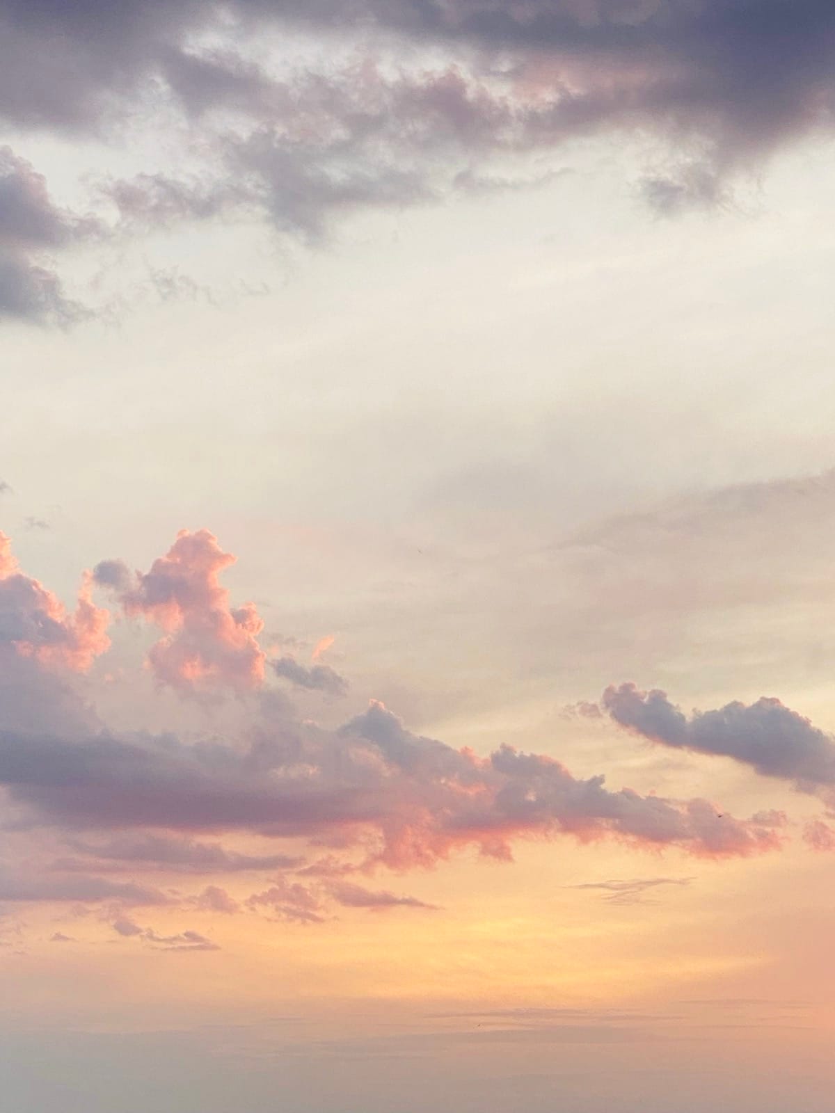 céu ao entardecer com nuvens volumosas em tons de rosa, laranja e roxo contra um fundo amarelo dourado