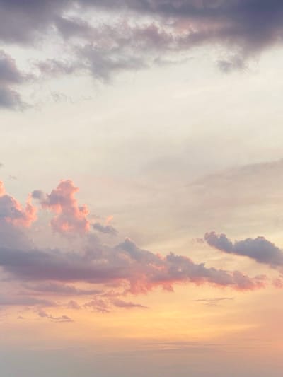céu ao entardecer com nuvens volumosas em tons de rosa, laranja e roxo contra um fundo amarelo dourado